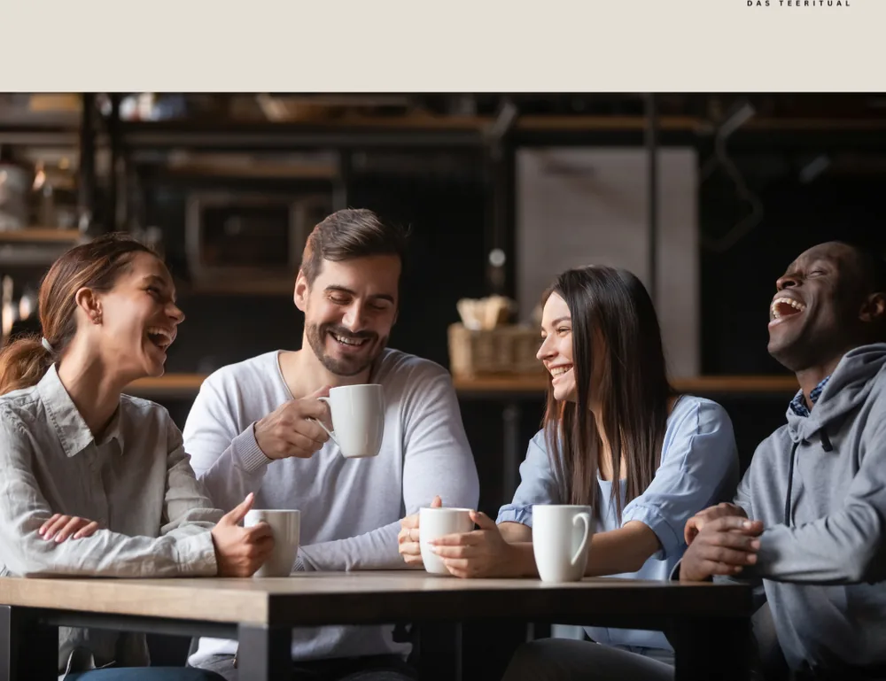 Vier Freunde lachen mit Teetassen am Tisch
